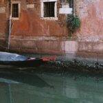 A black gondola sits stowed and covered at its mooring along a narrow canal. Image supplied.